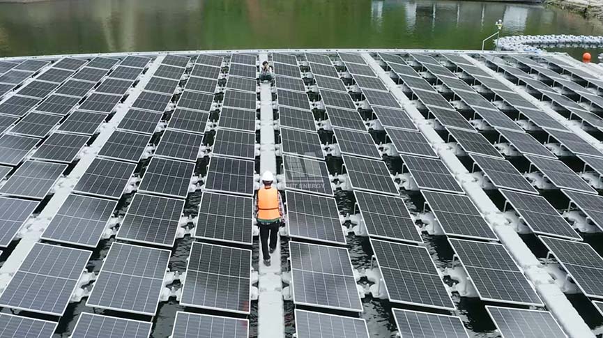 Worker walking on walkway between rows of floating solar panels (Mibet system)