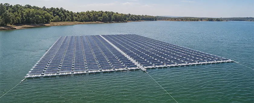 Utility-scale floating solar array on a reservoir, module rows spaced over open water with shore-anchored mooring.