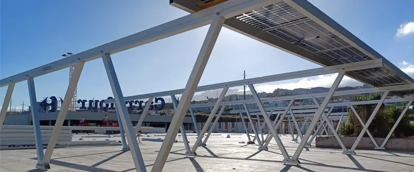Aluminum solar carport structure with angled support frames and photovoltaic panels over a commercial parking area.