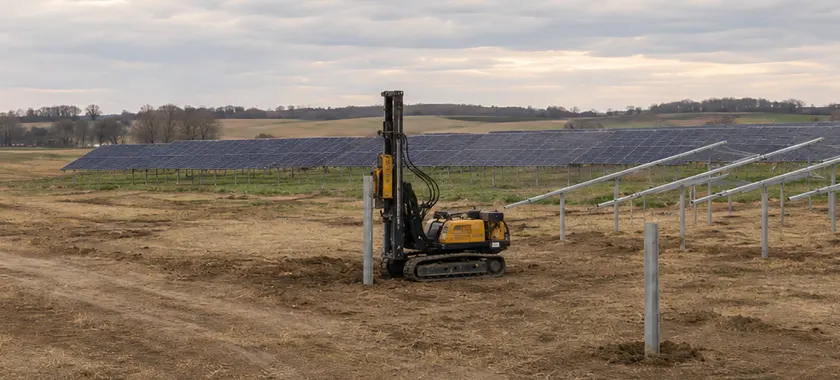 Pile driving rig installing a driven steel pile foundation for a fixed-tilt ground-mount solar array.