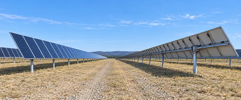 Aisle between rows of single-axis solar trackers, with module faces on the left and the torque tube, bearings and piles visible under the row on the right.